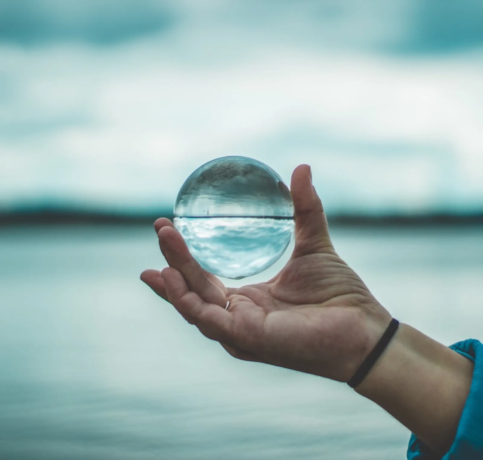 A hand holding a crystal ball that reflects a lake landscape
